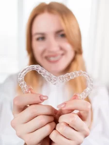 dental-caresmiling-girl-with-red-hair-holding-heart-shaped-aligners